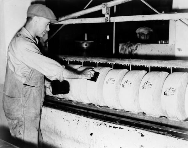 Dairy is a major industry in the State of Wisconsin. Pictured is a worker in 1922 at a New Glarus cheese factory placing a Wisconsin stamp on wheels of cheese.