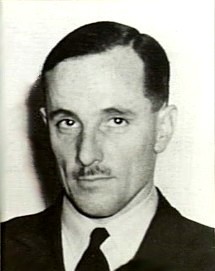 Head-and-shoulders portrait of dark-haired man with small moustache, wearing dark jacket and tie