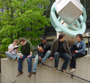 five young people sitting on stone wall in front of modern sculpture and tree