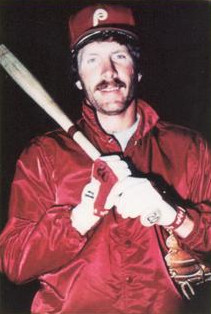 Mike Schmidt wears a red Phillies jacket and holds a bat on a his shoulder.