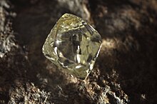 A clear octahedral stone protrudes from a black rock