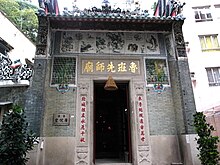The exterior of a temple, with a large door flanked by Chinese characters. Other urban buildings can be seen in the background.