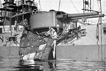 The side of the ship has been badly caved in by a large, bent piece of steel plate thrown by the explosion.
