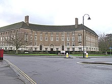 Red brick building with a curved façade seen across roads.