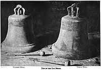 Two large church bells resting on a stone pavement, each carved with a indistinguishable inscription.