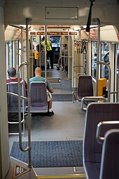 Interior of a streetcar, with several seats facing forwards and backwards, a two-step stairway, a yellow fare validation machine, and several poles.