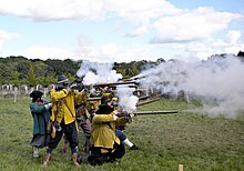 A colour photograph showing a re-enactment of a seventeenth century battle, with a unit of infantry firing muskets