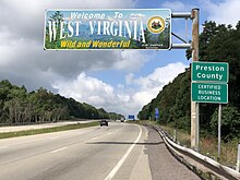 A sign above the highway reads "Welcome to West Virginia—Wild and Wonderful." An adjacent sign reads "Preston County. Certified Business Location."