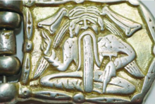A belt buckle depicting a long-haired sitting man