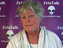 Nancy Lieder is seen from the neck up in front of a background of grey alien faces
