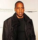 An Afro-American man wearing a black leather jacket and black t-shirt stands before a white background.