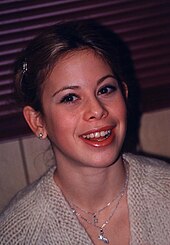 Caucasian young woman, in her late teens, with hair in bun, and bright red lipstick, smiling and looking upwards and to the left