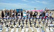 About 20 trans people kneeling with arms upraised behind black crosses with papers depicting cause of death taped to them erected for the trans people who were killed in 2016.