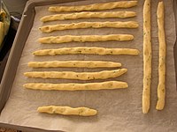 Unbaked home-made grissini on a baking tray, seasoned with herbs