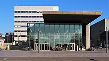 Blick auf das Eingangsgebäude der TU Darmstadt vom Karolinenplatz aus. Im Hintergrund sind das Audimax, das Karl-Plagge-Haus, das Verwaltungsgebäude und das Kongresszentrum Darmstadtium sichtbar,