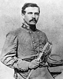 Black and white photo shows a young man with a moustache holding a sword in his right hand. He wears a Confederate general's uniform.