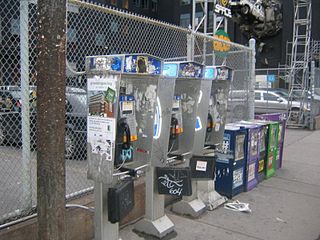 Toronto payphones covered with graffiti and notices. Telephone books are contained in weatherproof holders hanging from the bottom of each phone.
