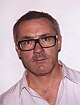 Damien Hirst, a man wearing glasses with brown rims, and a white shirt with faint vertical stripes