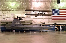 Starboard view of jet aircraft in museum among suspended aircraft and an American flag.