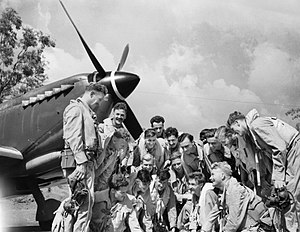 Group of men in flying suits talking in front of a single-engined aircraft