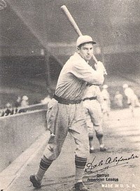 A black and white photograph of a baseball player posed with a bat swung behind his head