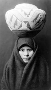Zuni Girl with Jar, c. 1903. Head-and-shoulders portrait of a Zuni girl with a pottery jar on her head.