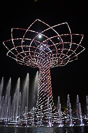 Large tree made of lights at night, surrounded by fountains