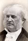 Bust portait photograph of an old man, mostly balded with whispy white hair at the edges of his head and mutton chops, wearing a high-collared dress shirt.