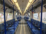 View down the interior of London Underground 1995 stock train in October 2018, with speckled light grey flooring, two-tone blue patterned seats and vertical dark blue hand rails