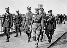A general walks in military uniform flanked by other officers
