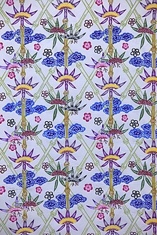 Fabric decorated with a busy design of diamonds constructed from light green bamboo stems and blue, pink and purple flowers on a white background.