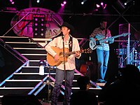 Singer Clay Walker strumming a guitar while singing into a microphone.