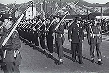 Soldiers in formal uniform with slouch hats, blancoed web belts, garters and slings being inspected on parade