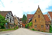 Photograph of the gate (left of center, background) and flanking buildings. The closest, on the right, is the Frühmesserhaus.