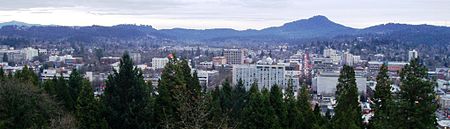 The flat-roofed buildings of downtown Eugene in front of Spencer Butte, a prominent forested hill