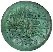 The obverse of a bluish green-colored glass piece inscribed in Arabic