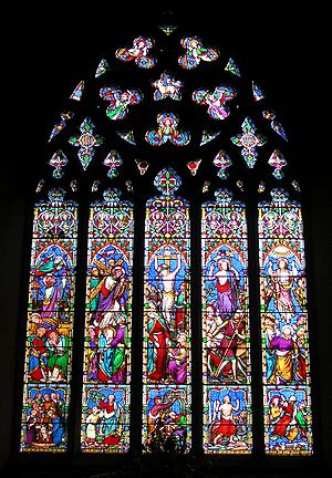 This stained glass window is divided into five long sections, above which the stone tracery looks like a lacey medallion. The colours are not like Medieval glass; there is a lot of bright red, pale blue, apple green, mauve and pink.