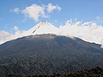 Snow-covered volcanic peak above green forests
