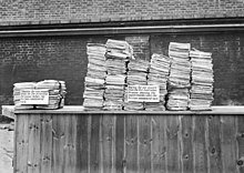 Black and white photograph of two stacks of documents on a table. The stack on the right is much larger than that on the left.