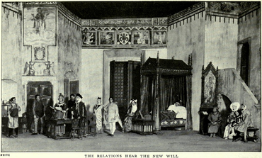 A black and white photograph of a stage set, featuring high walls and medieval Italian motifs. Seven men (two of them tradesmen), three women and a child, all in medieval dress, stand or sit around the room listening to an important-looking man who is reading a document aloud.