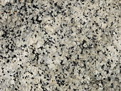 A closeup of the polished face of a slab of granite showing grains of white, bluish gray and black.