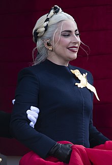 Side view of Lady Gaga wearing a navy blue dress decorated with a golden bird and smiling