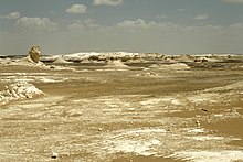 A picture of the White Desert in Egypt, with cliffs, dunes, and white chalk rock formations created through erosion by wind and sand