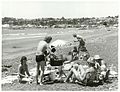 A group of people on a beach sitting around a barbecue grill.