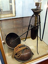 A glass display case holds a mechanical device with a lever arm, plus two metal hemispheres attached to draw ropes.