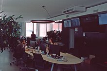 Newsdesk in der Redaktion in Zürich. Zu sehen sind zwei Menschen, die vor Computerarbeitsplätzen sitzen. An der Wand sind mehrere Bildschirme.