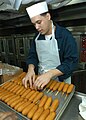 A sailor aboard the USS George Washington places corn dogs on a tray to be baked in the galley