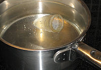 picture of a bell-shaped menstrual cup, covered in simmering water in a stainless cooking pot on a hob