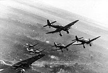 a black and white photograph of seven aircraft in flight over a smoky battleground