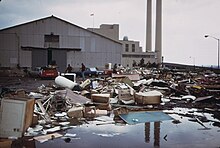 An industrial plant, with a mess of household trash items strewn haphazardly on the ground in front of it.